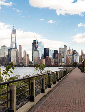 Waterfront walkway in Jersey City with paved stone path, views of Hudson River and Manhattan behind.