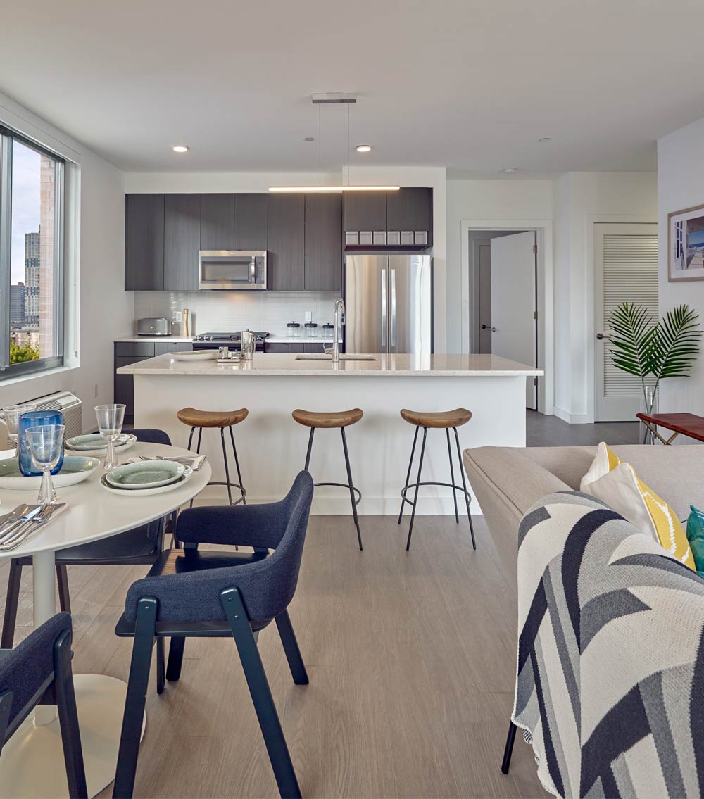 Model apartment living and dining room with couch, breakfast nook and bar seating at the counter.